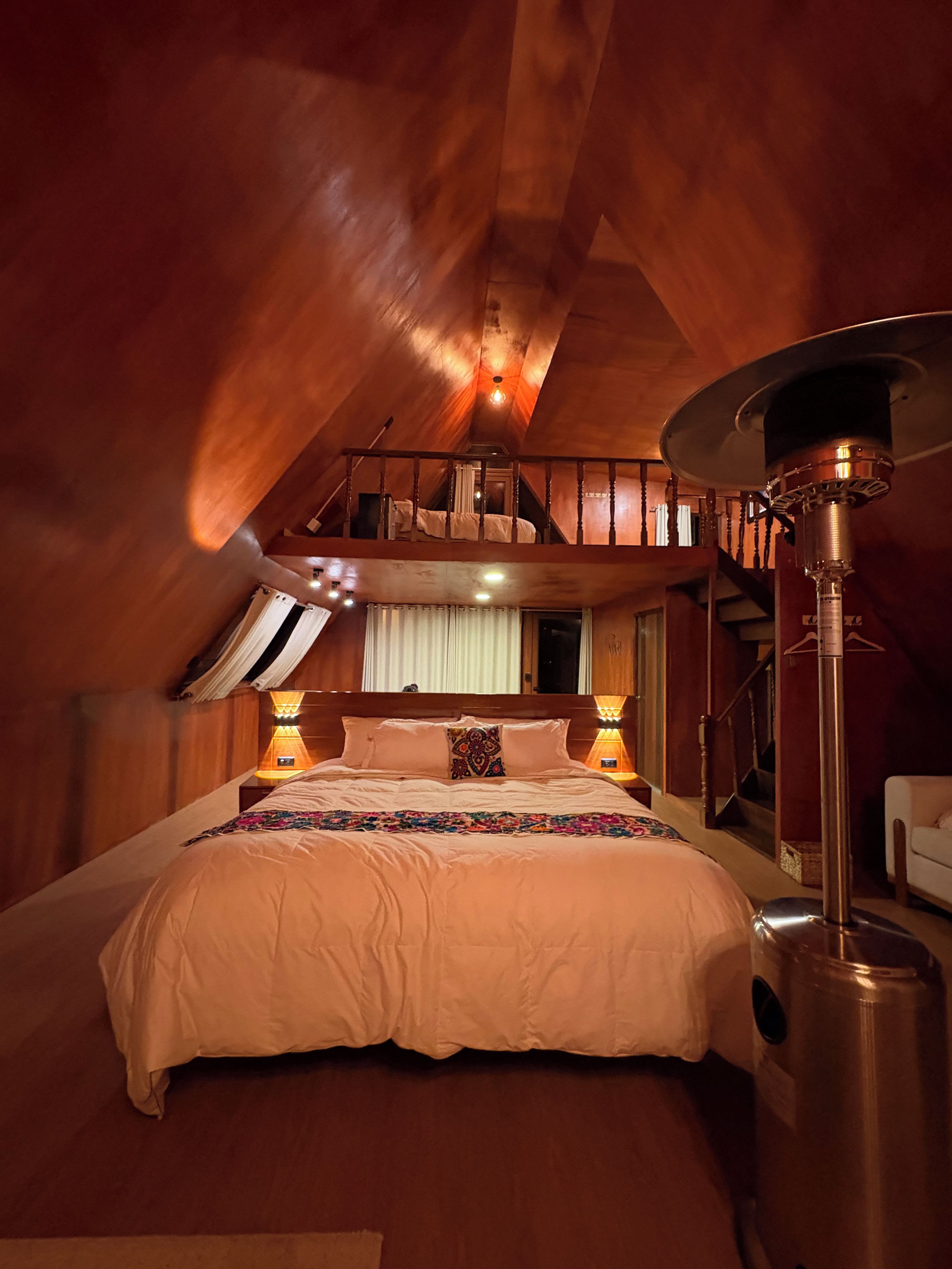 A bedroom with a large bed, a ceiling fan, and a staircase leading to an upper level.