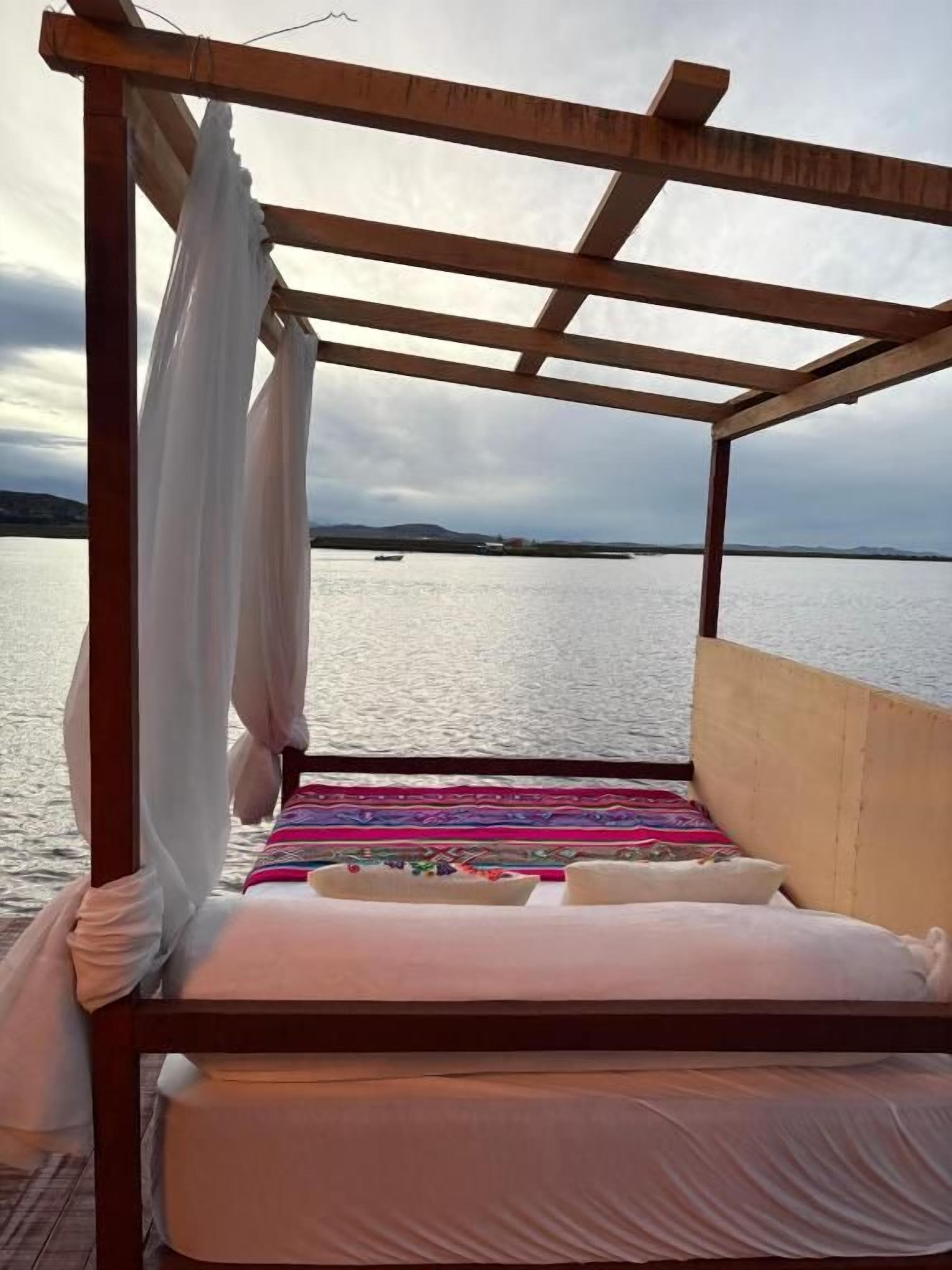 Uma cama com dossel, vista para a água e um barco ao longe.