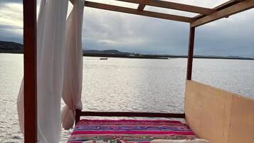Uma cama com dossel, vista para a água e um barco ao longe.
