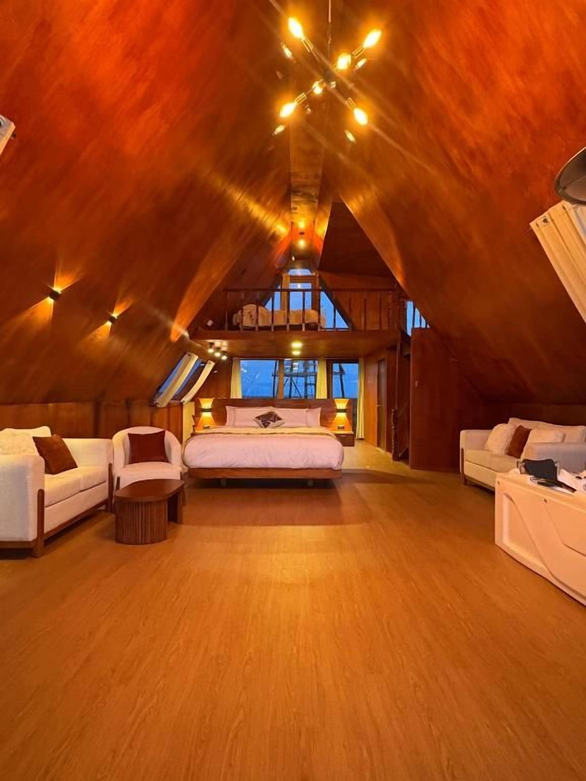 A spacious attic bedroom with a sloped ceiling, a large bed, two sofas, and a small table.