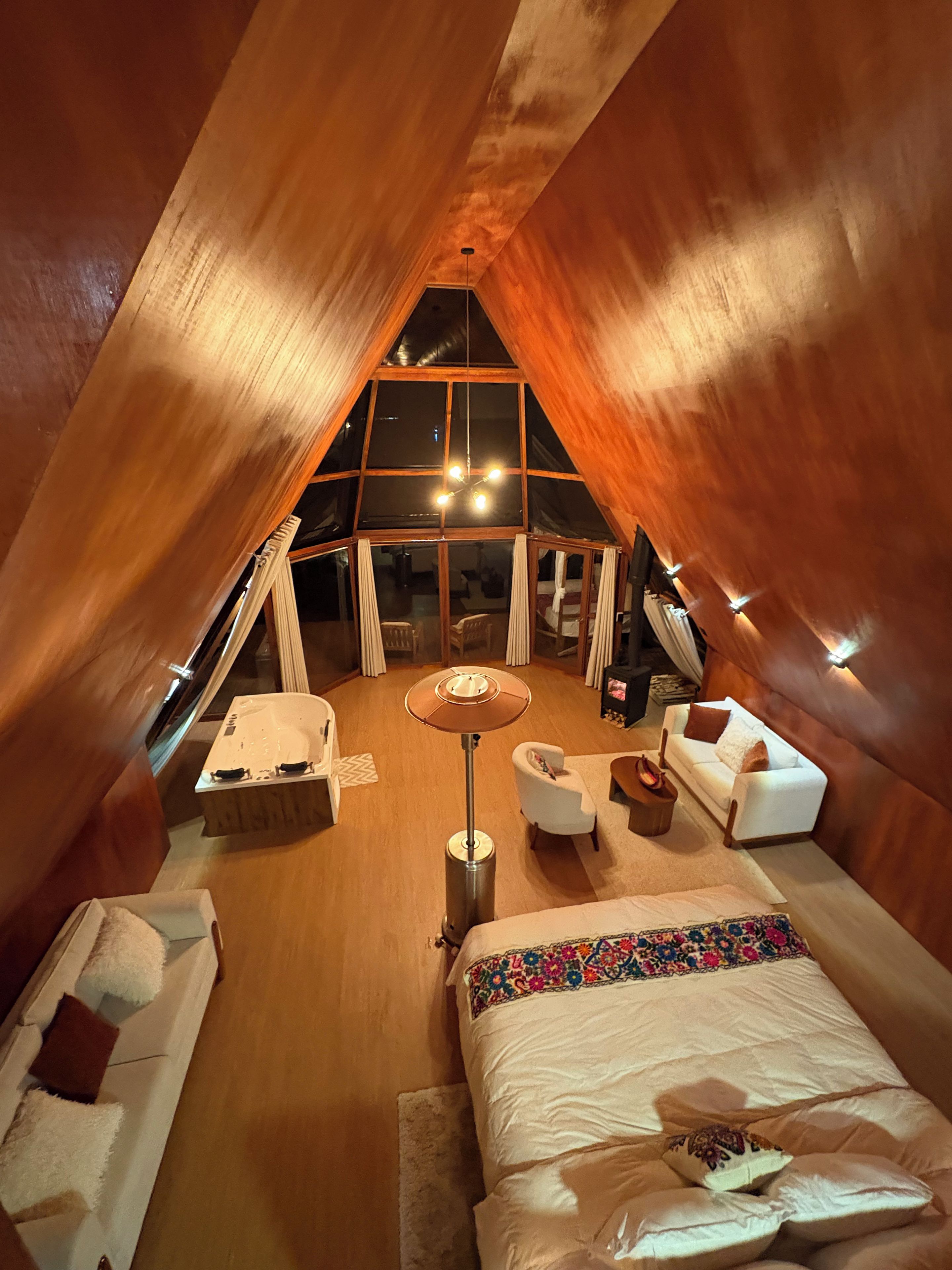 Un dormitorio cálido y luminoso en el ático, con una cama grande, una mesita pequeña y una silla.
