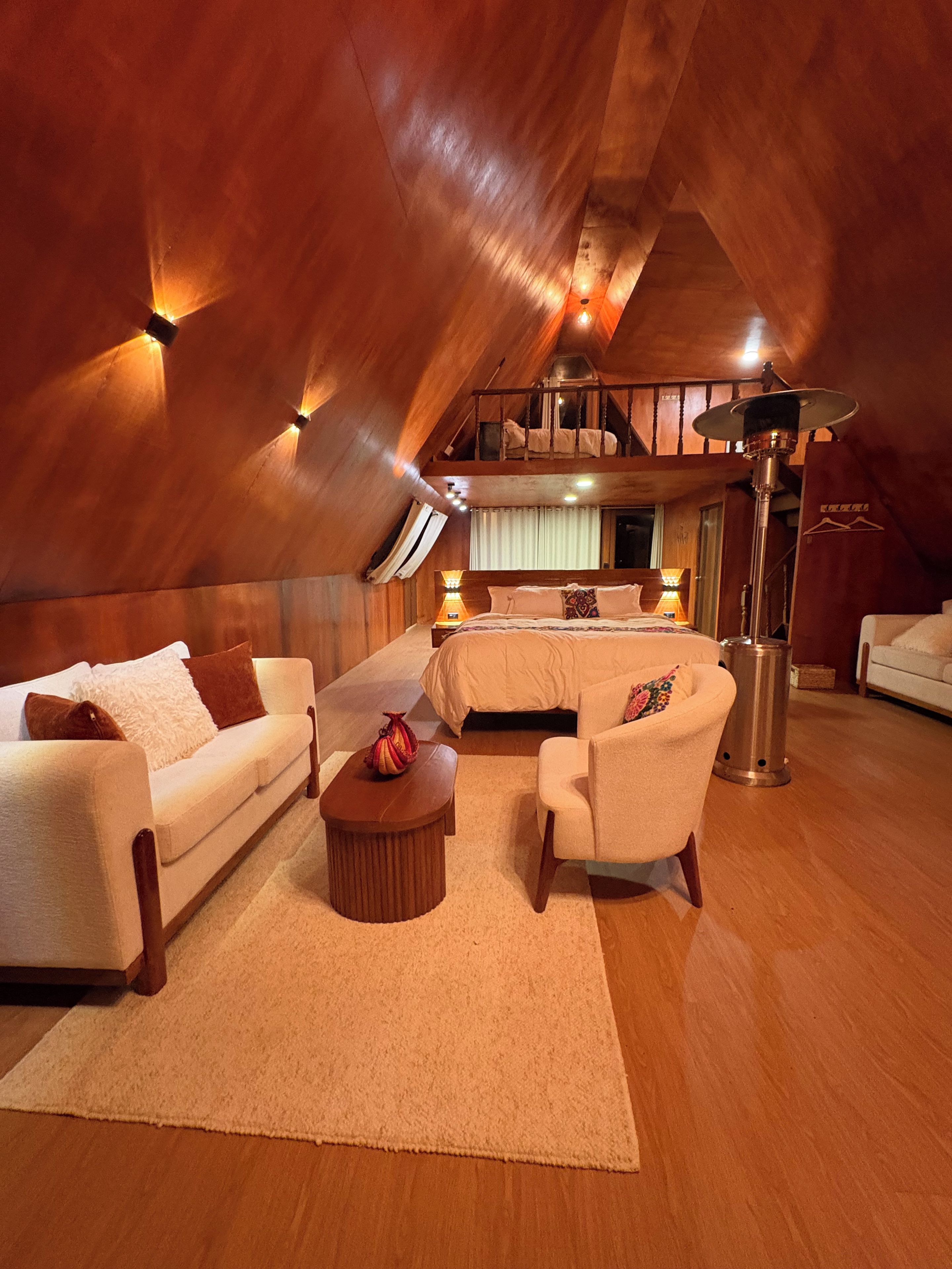 A spacious attic bedroom with a large bed, a sofa, a chair, and a coffee table.