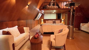 A spacious attic bedroom with a large bed, a sofa, a chair, and a coffee table.