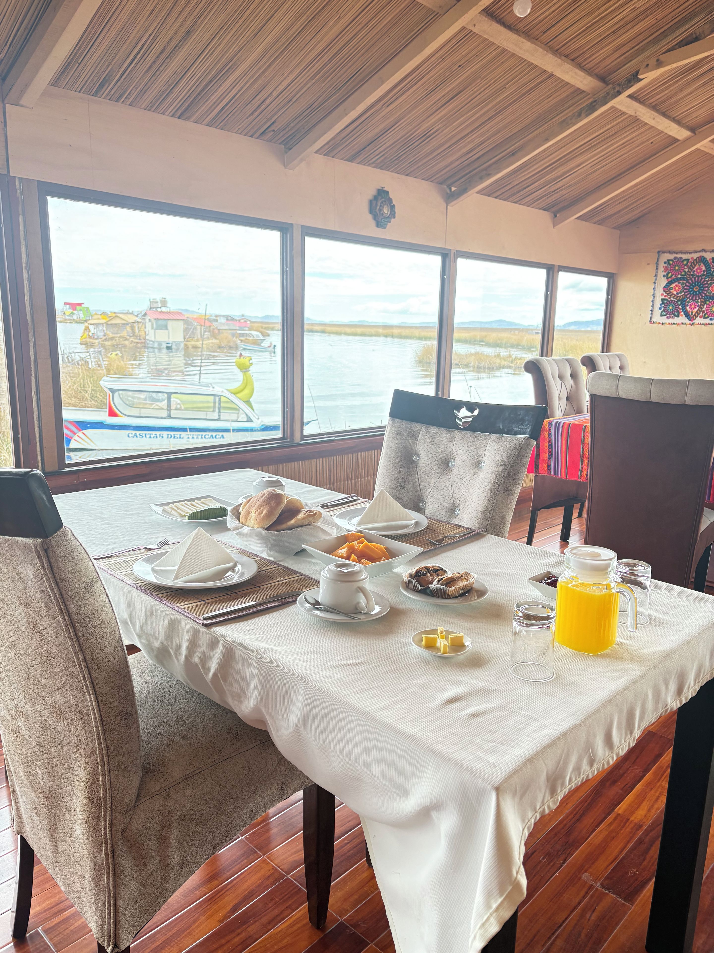 A dining area with a table set for breakfast, overlooking a water body with boats.