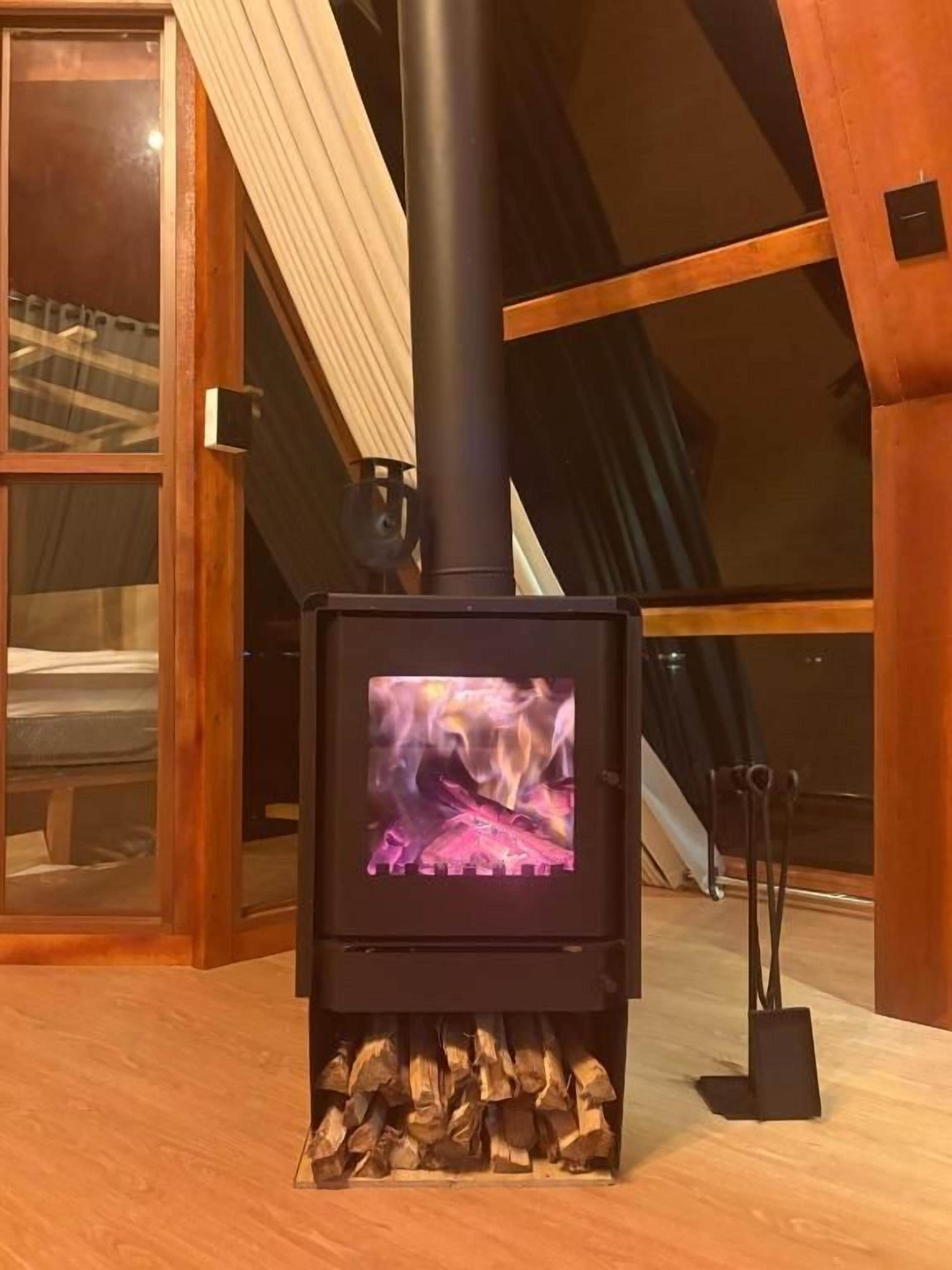 Una estufa de leña con fuego a la vista, ubicada en una habitación con techo inclinado y vigas de madera.