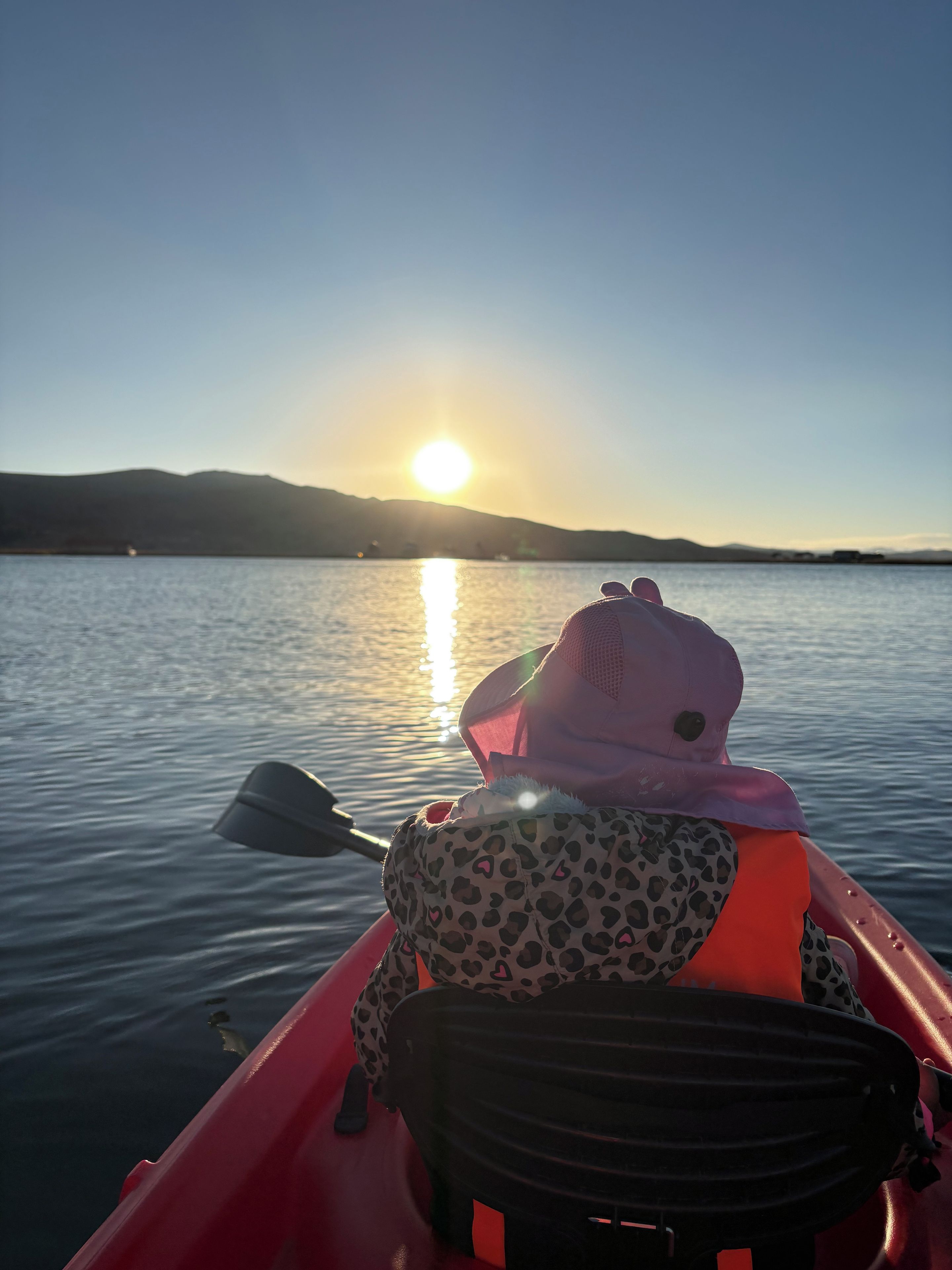 A person in a kayak on a calm body of water with a sunset in the background.