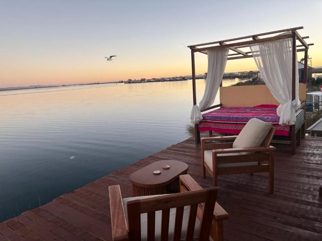 A wooden deck with a bed and chairs overlooking calm water.