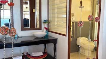 A bathroom with a black vanity, a white sink, and a mirror. There are decorative hanging items and a window with blinds.