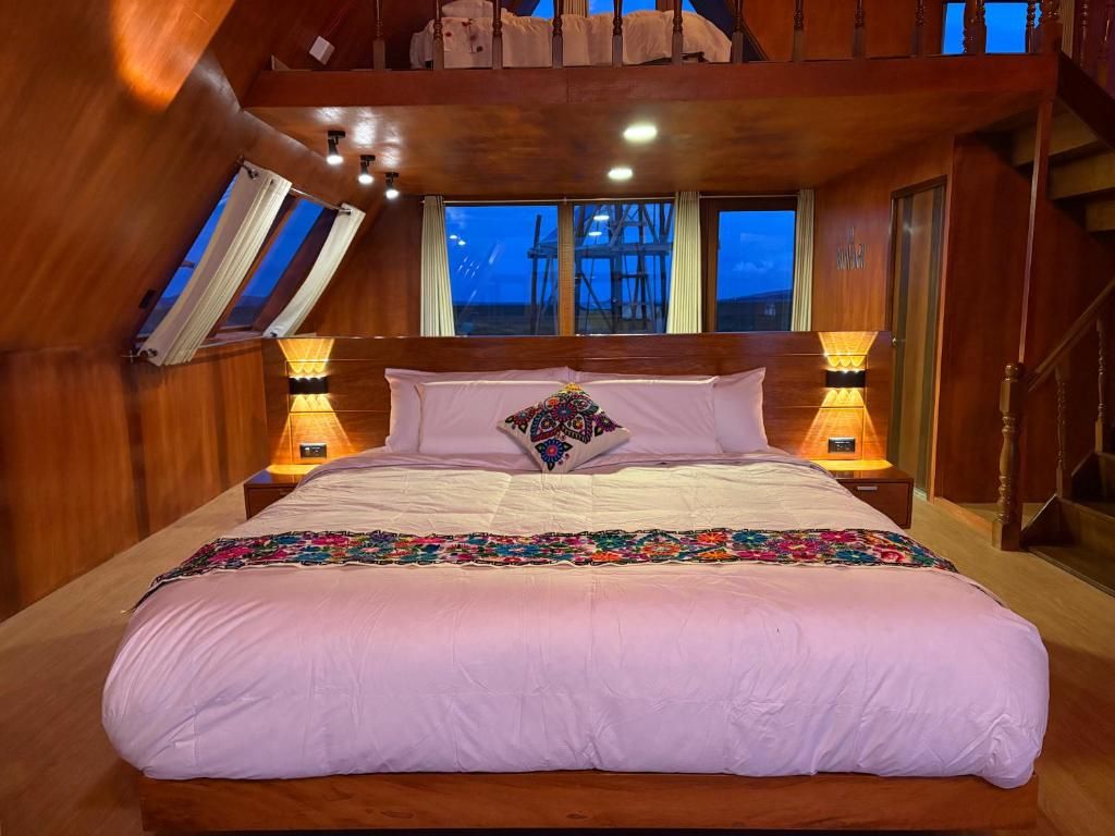 A bedroom with a large bed, two bedside lamps, a window, and a wooden ceiling.