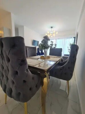 A dining area with a table set for four, upholstered chairs, a vase with a plant, and a chandelier. - Stylish Metropolitan 2 Bedroom Apartment (Santo Domingo)