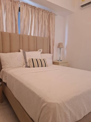A neatly made bed with a headboard, a bedside lamp, and a nightstand. - Stylish Metropolitan 2 Bedroom Apartment (Santo Domingo)