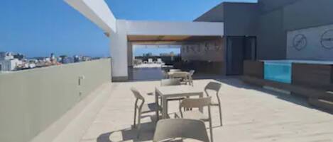 Un patio al aire libre con mesa y sillas, vista al mar y un edificio de diseño moderno.