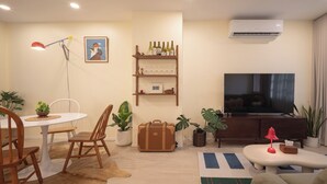Una sala de estar con televisor, una mesa de comedor con sillas, un sofá y una mesa baja.