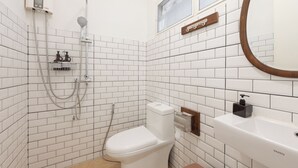 Un baño con azulejos blancos tipo metro, inodoro blanco, ducha con cabezal de ducha manual, toallero y espejo con marco de madera.
