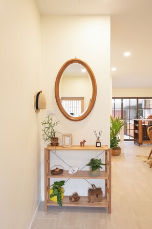 A hallway with a wooden console table displaying various items, a round mirror on the wall, and a view into the adjacent room. - Private2BR Townhome in the Heart of Nimman  Perfect for Families &Groups+parking (Chang Wat Chiang Mai)