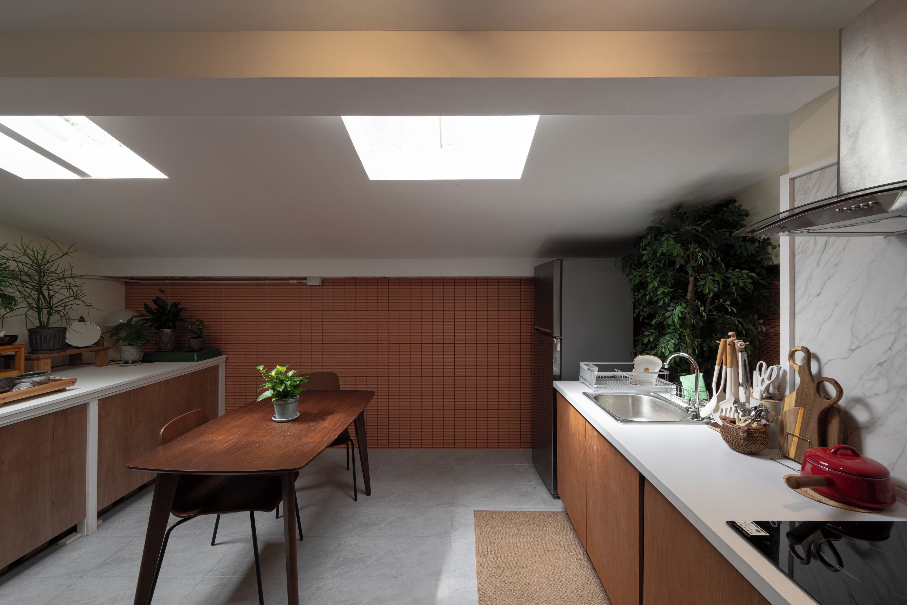 A modern kitchen with a dining area, featuring a wooden table, potted plants, and a built-in oven.