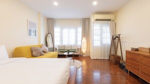 Habitación de hotel con cama, sofá, sillón, mesa, espejo, cómoda y aire acondicionado.