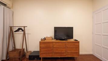 Ein Zimmer mit einem Holzkabinett, einem Fernseher darauf, einer Fernbedienung und einer kleinen Schachtel auf dem Kabinett.