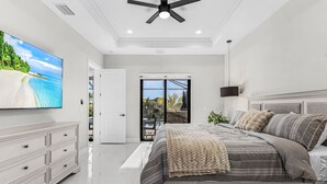 Un dormitorio con cama, televisión, ventilador de techo y vista a una piscina.