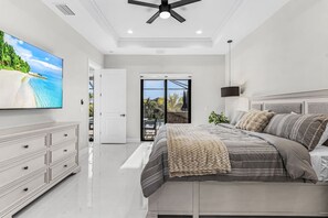 A bedroom with a bed, a TV, a ceiling fan, and a view of a pool. - Villa du Soleil | Luxury, Pool & Palm Dreams (Cape Coral)