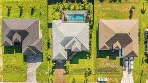 Un área residencial con tres casas, cada una con un diseño de techo diferente, rodeada de céspedes cuidados y palmeras.