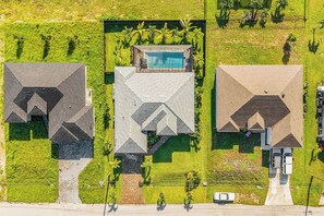 A residential area with three houses, each with a distinct roof design, surrounded by well-maintained lawns and palm trees. - Villa du Soleil | Luxury, Pool & Palm Dreams (Cape Coral)