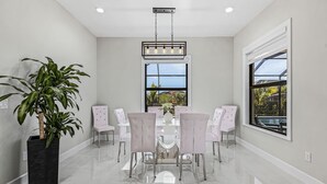 Comedor con mesa y sillas blancas, un ventanal con vistas y una lámpara colgante.