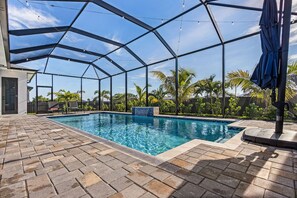 A covered outdoor swimming pool with a clear blue sky, surrounded by palm trees and a brick patio. - Villa du Soleil | Luxury, Pool & Palm Dreams (Cape Coral)