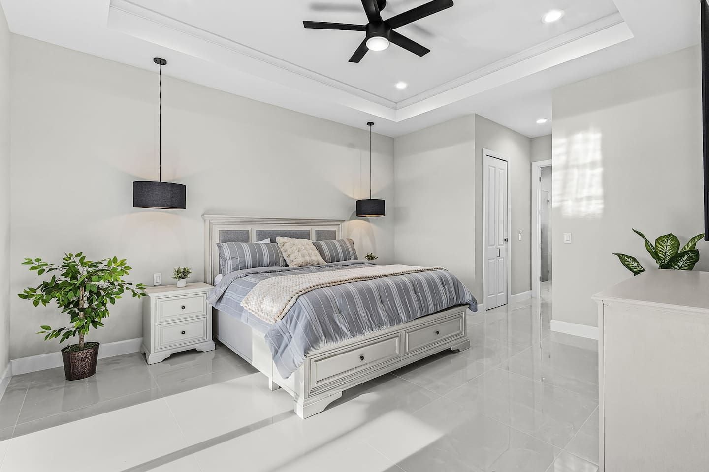 A modern bedroom with a large bed, bedside tables, a ceiling fan, and a potted plant.
