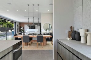 A modern kitchen with a dining area, large windows, and a view of the outdoors. - Round Valley Residence (Sherman Oaks)