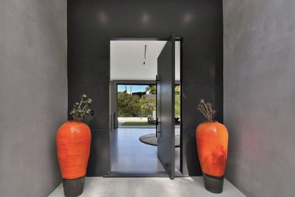 A modern hallway with a glass door leading to an outdoor area, flanked by two orange vases with dried plants. - Round Valley Residence (Sherman Oaks)