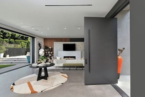 A modern living room with a fireplace, a television mounted on the wall, and a dining area with a round table and chairs. - Round Valley Residence (Sherman Oaks)