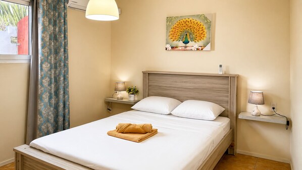 A hotel room with a bed, two bedside tables, a lamp, a painting, and a window with curtains.