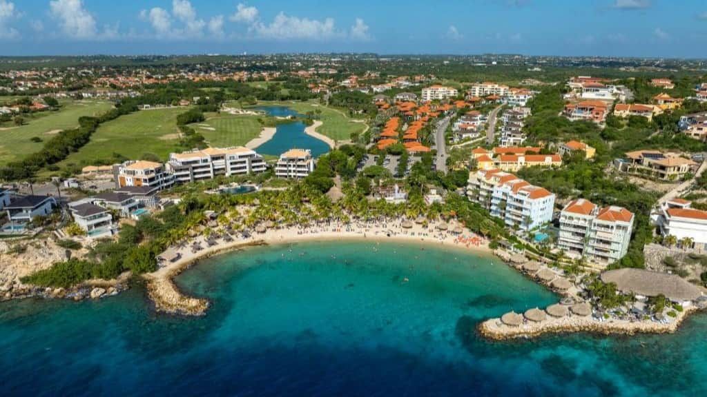 An aerial view of a coastal resort with beachfront properties, a marina, and a golf course.