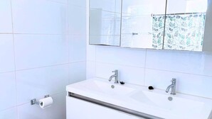 A modern bathroom with a white sink, two faucets, a toilet, and a mirror. - Fully Air-Conditioned| Central | Near Beachess (Willemstad)