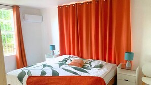 A bedroom with a bed, orange curtains, a bedside table with a lamp, and a window with curtains. - Fully Air-Conditioned| Central | Near Beachess (Willemstad)