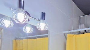 A bathroom with a yellow shower curtain, a wall-mounted light fixture, and a ceiling fan. - Apartment Near Beaches, Dining & Attractions (Willemstad)