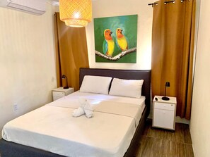 Ein Hotelzimmer mit einem Bett, zwei Nachttischen, einer Lampe, einem Vogelgemälde und einem Vorhang.