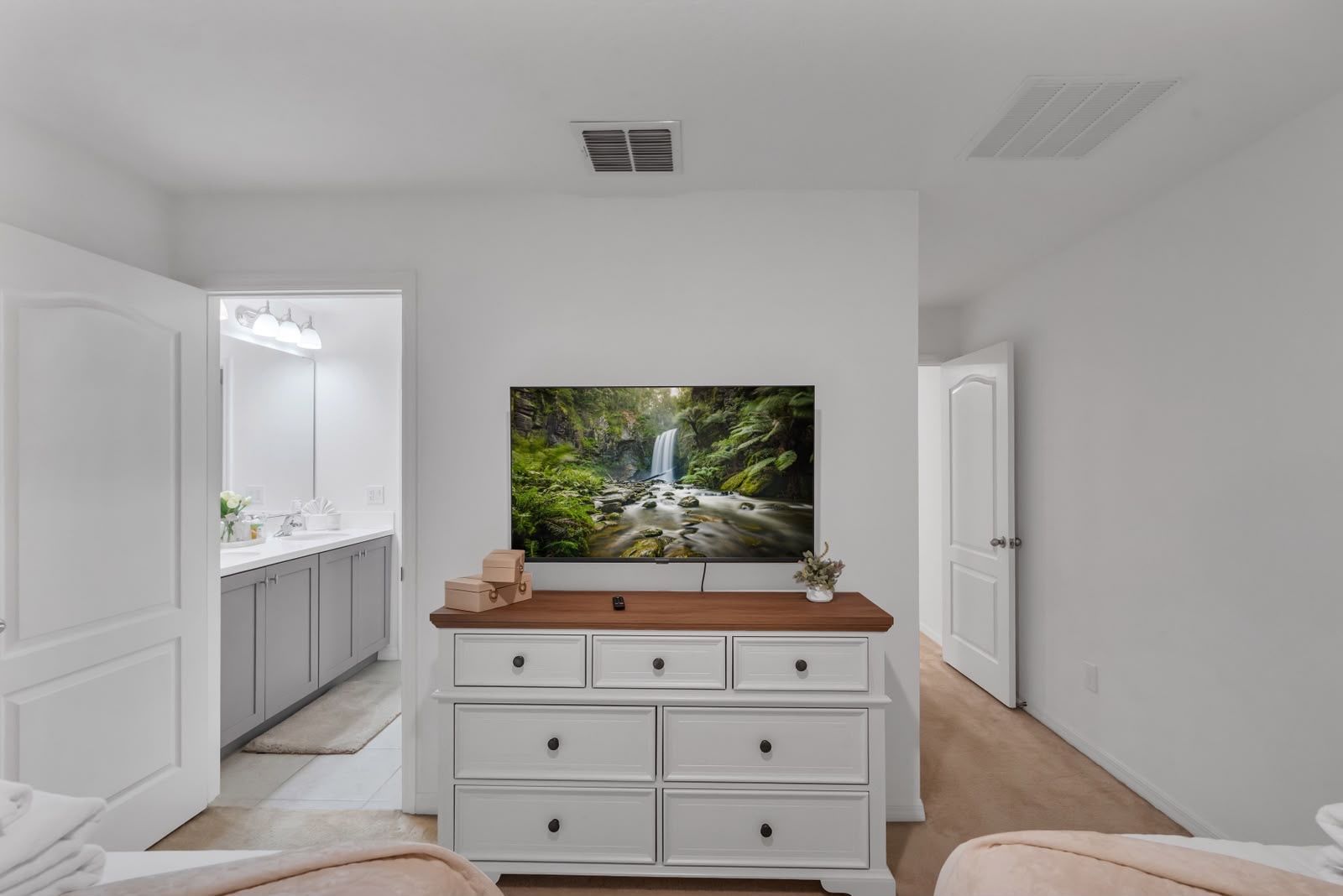A bedroom with a large bed, a dresser with drawers, a mirror, and a painting of a waterfall on the wall.