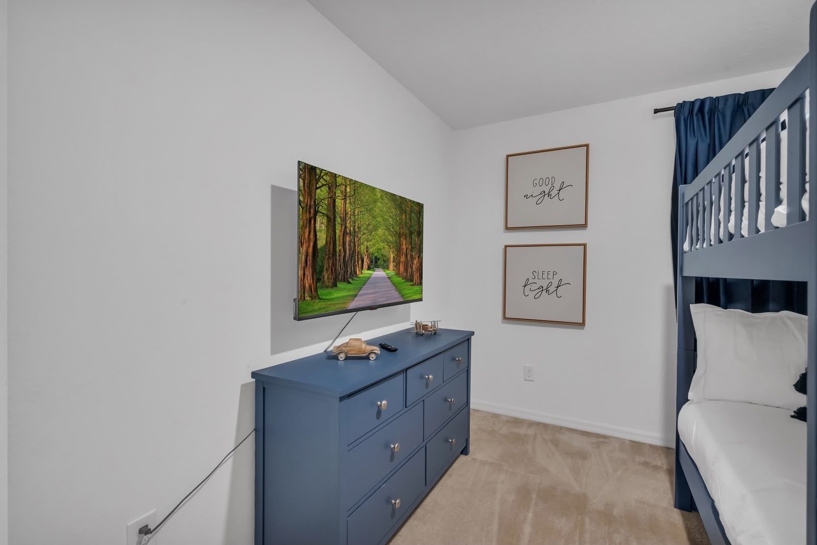 Quarto com cama beliche, televisão na parede, cômoda e duas frases motivacionais emolduradas.