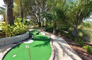 En miniatyrgolfbana med en grön yta för att putta på, ett hål med nummer och träd runt omkring.