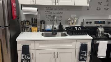 A kitchen with white cabinets, stainless steel appliances, and kitchenware. There are two mats on the floor with kitchen-related text.