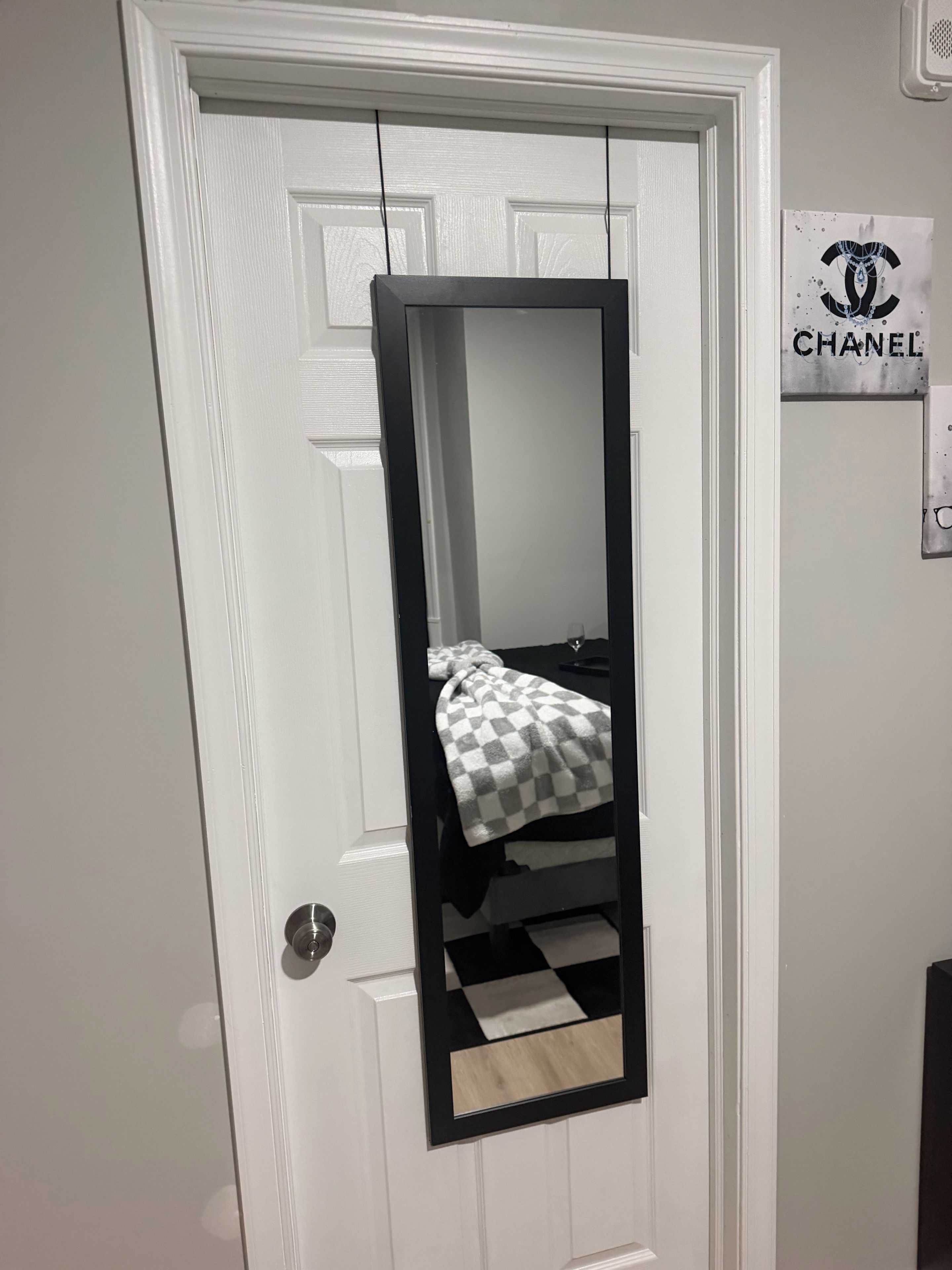 A door with a mirror reflecting a bed with a checkered blanket.