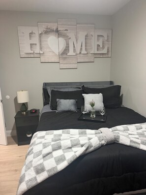 Un dormitorio con una cama, una mesita de noche, una lámpara y una decoración de pared que dice 'HOME'.