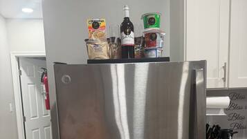 A stainless steel refrigerator in a kitchen with a white door and a fire extinguisher in the background.