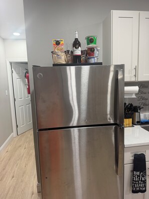 Ein Edelstahl-Kühlschrank in einer Küche mit einer weißen Tür und einem Feuerlöscher im Hintergrund.