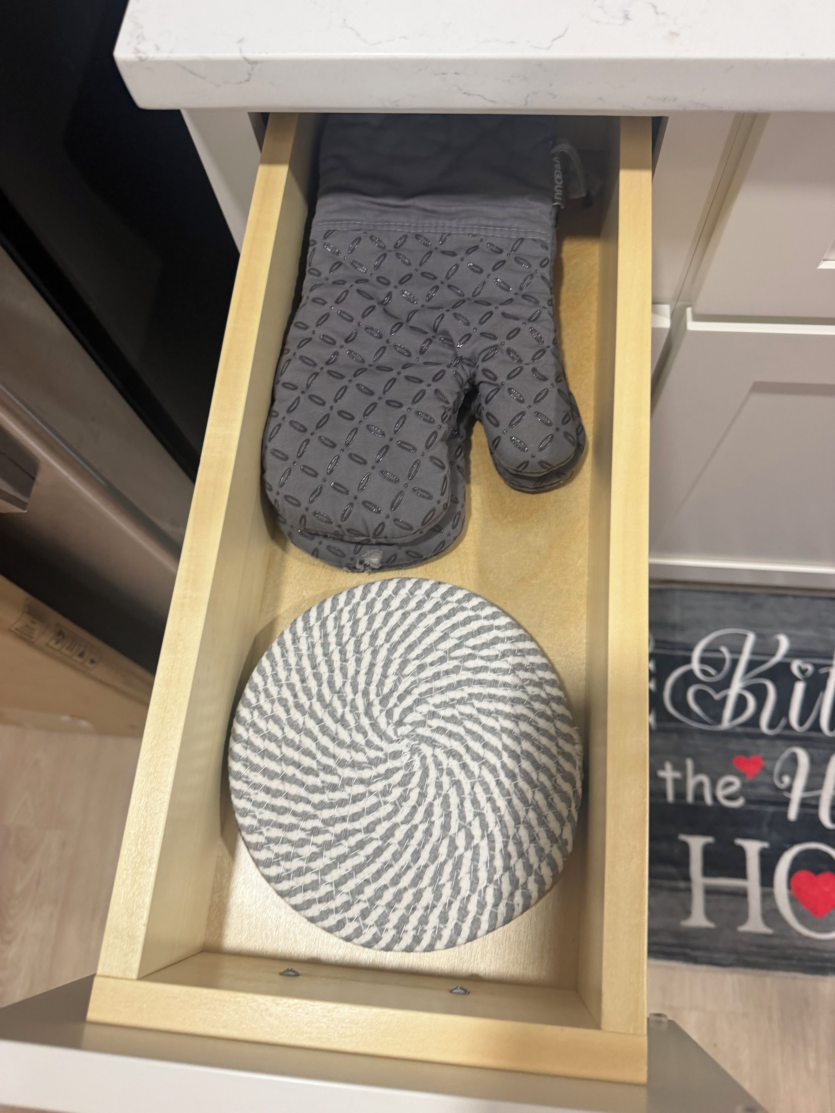 A drawer containing a black oven mitt and a circular woven mat.