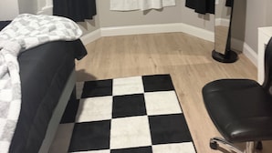 A room with a bed, a chair, a standing lamp, and a checkered rug.