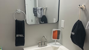A bathroom with a white sink, a mirror, and a towel rack with a 'HOME' towel.
