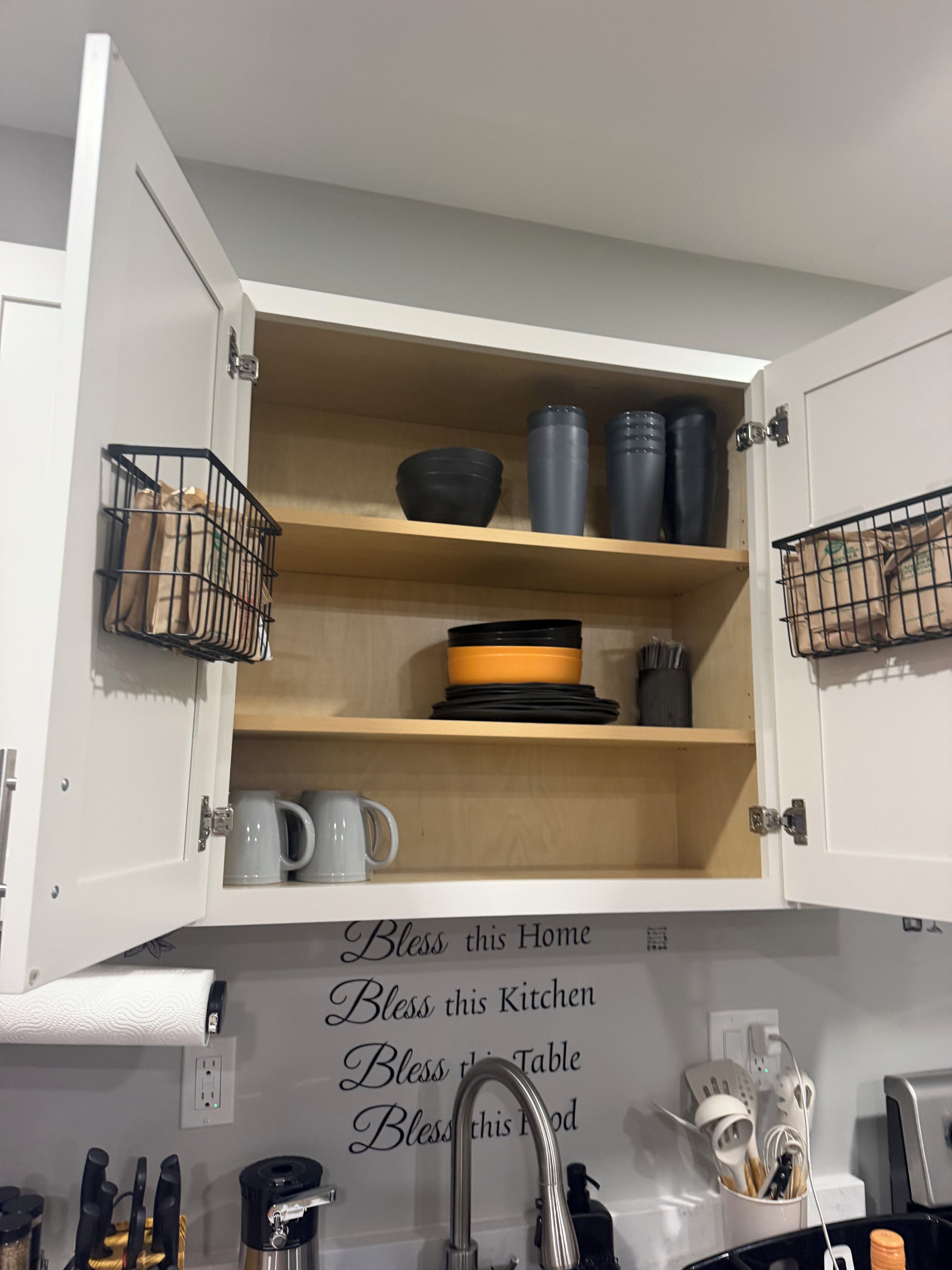 A kitchen with open cabinets displaying kitchenware and a sign with blessings for the home and kitchen.